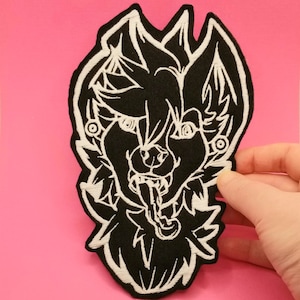 May include: Black and white embroidered patch of a snarling wolf with a tongue sticking out. The wolf has a white outline and is set against a black background.