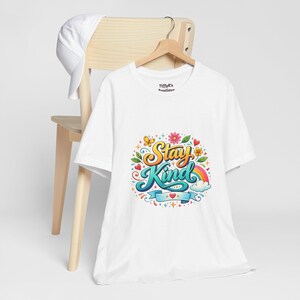 Camiseta branca com estampa floral colorida "Stay Kind" (Mantenha a Gentileza) | Mensagem positiva e design com arco-íris
