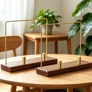 May include: Two rectangular wooden display stands featuring a tall, thin, gold-toned metal arch frame and a small gold-toned metal peg on the base. The wooden base of the left stand is engraved with the name David, and the right with Leonard.