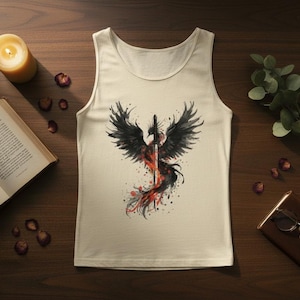 K&ouml;nnte beinhalten: Cremefarbenes Tanktop mit einem schwarzen und roten Ph&ouml;nix-Design mit einem Schwert. Die Grafik hat einen Aquarelleffekt. Das Oberteil liegt auf einer Holzoberfl&auml;che mit einer brennenden Kerze, einem Buch und anderen dekorativen Elementen.