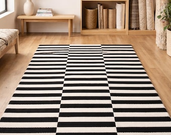 May include: A rectangular area rug with a bold black and white striped pattern. The rug is made of a soft, woven material and is placed on a hardwood floor. The design features horizontal stripes that alternate in color.