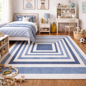 Könnte beinhalten: Kinderzimmer mit einem blau-weißen geometrischen Teppich. Das Zimmer verfügt über ein Bett mit blauer Bettwäsche, einen weißen Schreibtisch und zwei gerahmte Tierporträts. Ein Spielzeugeisenbahn und ein Korb mit Spielzeug liegen auf dem Boden.
