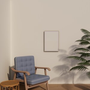 May include: A light blue upholstered armchair with wooden arms and legs. A small, round, woven side table is in front of the chair. A framed, blank picture hangs on the wall. A potted plant is to the right.