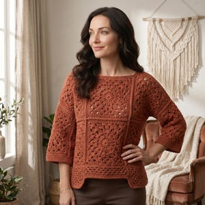 May include: A terracotta-coloured, crocheted jumper with a square neckline and three-quarter sleeves. The jumper features a detailed floral pattern in the centre and on the sleeves. The garment is made of a soft, textured yarn, perfect for a cosy, handmade look.