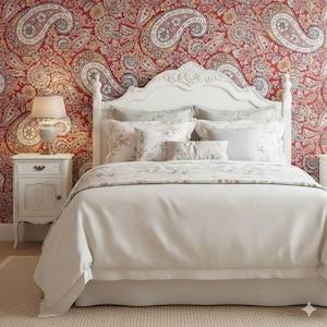 Può includere: Una scena di camera da letto con un letto bianco, biancheria da letto color crema e cuscini floreali. Un comodino con una lampada è posizionato accanto al letto. La parete è rivestita con una carta da parati paisley rossa, creando un'atmosfera accogliente.