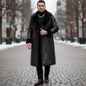 May include: A long, black, faux-leather coat with a crocodile pattern. The coat features a dark brown fur collar and cuffs. The person is wearing a black turtleneck and black pants. A silver watch and chain are visible.
