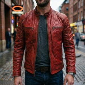 May include: A red leather jacket with a snakeskin texture. The jacket has a zipper closure, two chest pockets, and a stand-up collar. The person is wearing a gray t-shirt and blue jeans. A watch is visible on the wrist.