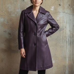 May include: A plum-colored leather coat with a classic design. The coat features a notched collar, three black buttons, and a tailored fit. The coat is knee-length and has long sleeves.