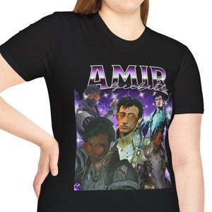 Puede incluir: Camiseta negra con un diseño gráfico retro. El diseño presenta el nombre "AMIR" en morado, sobre un collage de imágenes de personas. El conjunto tiene una estética vintage.