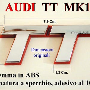 Puede incluir: Un emblema cromado Audi TT MK1 con detalles rojos. El emblema mide 3,5 cm de alto, 7,9 cm de ancho y 1,3 cm de grosor. El texto "AUDI TT MK1" se muestra encima del emblema.