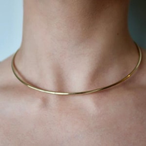 Peut inclure: Un collier ras du cou doré simple et élégant. Le collier est une fine bande incurvée qui se porte près du cou. La couleur dorée donne au collier un aspect classique et polyvalent, adapté à diverses tenues et occasions.