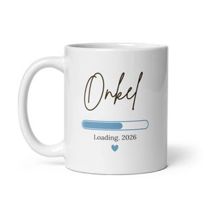 Może przedstawiać: Biały ceramiczny kubek z napisem "Onkel" w stylu odręcznym, paskiem ładowania, tekstem "Loading. 2026" i niebieskim sercem. Kubek ma zakrzywiony uchwyt i jest przeznaczony do gorących napojów.