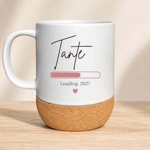 Könnte beinhalten: Weißer Keramikbecher mit Korkboden. Der Becher zeigt das Wort "Tante" in handschriftlicher Schrift, einen Ladebalken, das Jahr 2027 und ein kleines rosa Herz. Der Becher hat einen gebogenen Griff.