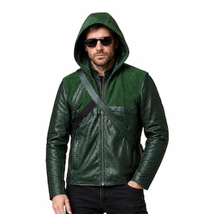 May include: A dark green hooded jacket featuring a combination of smooth leather and textured suede panels on the shoulders and chest. The jacket includes a full-length front zipper, long sleeves, and a diagonal black strap worn across the torso.