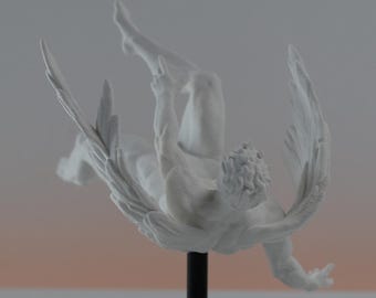 May include: A white matte sculpture of a winged figure in a falling or diving pose, mounted on a thin black vertical rod attached to a circular black base. The figure features detailed wings and a textured head, presented as a singular object.