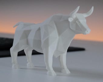 May include: A white, geometric, low-poly style bull figurine standing in a profile orientation. The sculpture features sharp, angular facets and clean lines, creating a modern, faceted appearance. The bull is depicted in a standing position.