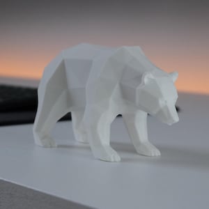 Può includere: Una statuetta di orso bianco caratterizzata da un design geometrico low-poly con sfaccettature angolari nette. L'orso è raffigurato in una posa eretta e in cammino con la testa leggermente abbassata, mostrando una superficie opaca e pulita.