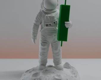 May include: A white astronaut figurine standing on a textured lunar surface base. The astronaut wears a detailed space suit with a smooth helmet and holds a tall, rectangular green candlestick chart marker in one hand, positioned upright.