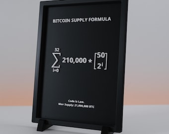 May include: A black framed sign displays the "BITCOIN SUPPLY FORMULA" in white text. The formula includes mathematical symbols and numbers. Below the formula, the text "Code is Law. Max Supply: 21,000,000 BTC" is printed in white.