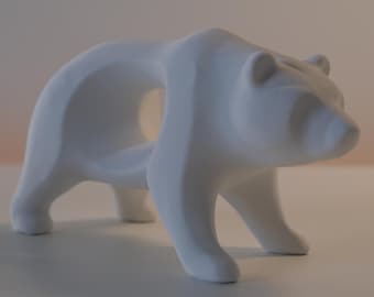 May include: A matte white bear figurine featuring a stylized, geometric design with a hollow opening in the center of its body. The sculpture is depicted in a standing position, showcasing smooth, clean lines and a solid, opaque white finish throughout.