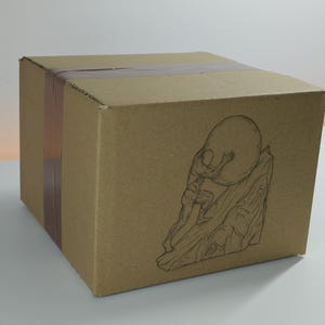 May include: A brown cardboard shipping box sealed with brown packing tape. The front panel features a black line art illustration of a figure pushing a large circular boulder up a steep, rocky incline, capturing a dynamic and detailed scene.