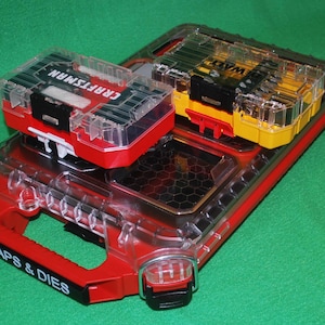 Może przedstawiać: Czerwony i przezroczysty plastikowy organizer na narzędzia z wieloma przegródkami. Organizer ma uchwyt i napis "TAPS & DIES". Dwa mniejsze pojemniki na narzędzia są ułożone jeden na drugim, jeden czerwony z napisem "CRAFTSMAN", a drugi żółty z czarnymi akcentami.