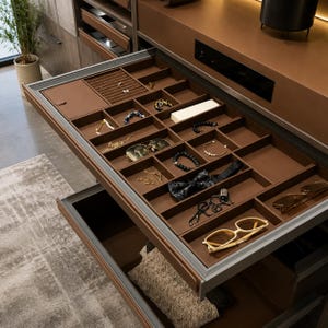 May include: A brown drawer organizer with multiple compartments containing various accessories including jewelry, bracelets, a bow tie, and two pairs of eyeglasses. The organizer is made of a smooth brown material and features a velvet-lined ring tray.