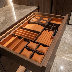 Könnte beinhalten: Offene Schmuckschublade aus Holz mit verschiedenen Fächern und orangefarbenem Lederfutter. Die Schublade hat Bereiche für Uhren, Ringe und andere Schmuckstücke. Die dunkle Holzschublade hat ein modernes Design und ist geöffnet, um ihren Inhalt zu zeigen.