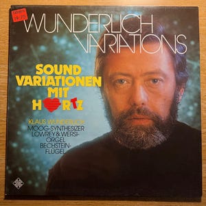 May include: A vintage vinyl record album cover featuring Klaus Wunderlich. The album title, "Wunderlich Variations," is in white, stylized text. The cover includes the text "Sound Variationen Mit Hertz" and a portrait of a man with a beard.