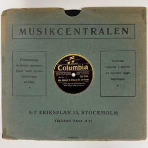 May include: Vintage record sleeve with the text "MUSIKCENTRALEN" at the top. A Columbia record is centered, featuring text and a musical note logo. The sleeve has additional text in Swedish, and is a muted green color.