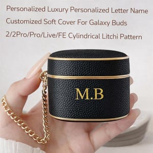 May include: Black, textured Galaxy Buds case with gold trim and a gold chain. The case has the initials "M.B" in gold lettering. The text on the image reads "Personalized Luxury Personalized Letter Name Customized Soft Cover For Galaxy Buds 2/2Pro/Pro/Live/FE Cylindrical Litchi Pattern."