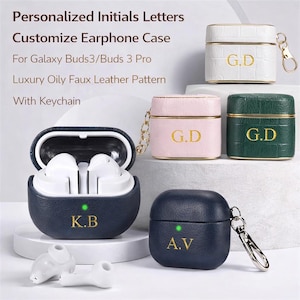 May include: Earphone cases in white, pink, and green, each with gold initials. A navy blue case is open, revealing white earbuds. The text reads "Personalized Initials Letters Customize Earphone Case For Galaxy Buds3/Buds 3 Pro Luxury Oily Faux Leather Pattern With Keychain."