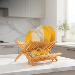 Puede incluir: Un escurreplatos de madera clara con platos amarillos y blancos y tazas amarillas. El escurreplatos est&aacute; colocado sobre una encimera blanca. El fondo muestra una cocina con armarios blancos y una ventana.