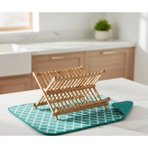 Puede incluir: Un escurreplatos de madera con dise&ntilde;o plegable, colocado sobre un tapete de secado con estampado turquesa y blanco. El estante est&aacute; hecho de madera clara y est&aacute; dise&ntilde;ado para sostener platos y otros utensilios de cocina. La alfombrilla tiene un patr&oacute;n geom&eacute;trico.