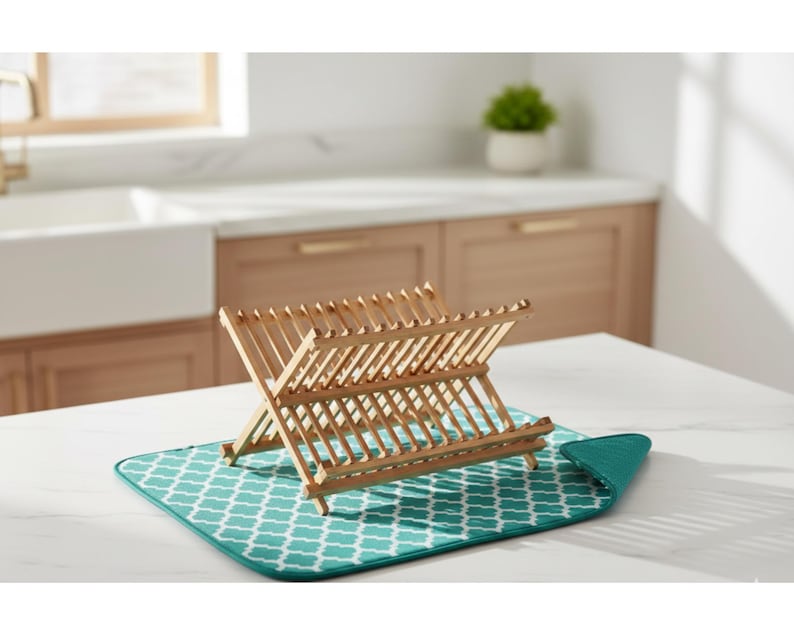 Puede incluir: Un escurreplatos de madera con dise&ntilde;o plegable, colocado sobre un tapete de secado con estampado turquesa y blanco. El estante est&aacute; hecho de madera clara y est&aacute; dise&ntilde;ado para sostener platos y otros utensilios de cocina. La alfombrilla tiene un patr&oacute;n geom&eacute;trico.