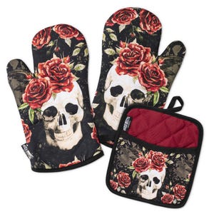 Könnte beinhalten: Zwei Ofenhandschuhe und ein quadratischer Topflappen mit schwarzem Hintergrund und einem wiederkehrenden Muster aus weißen menschlichen Schädeln, die mit leuchtend roten Rosen und grünen Blättern verziert sind. Jedes Teil hat einen schwarzen Rand.