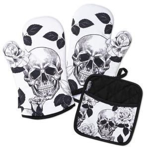 Puede incluir: Un juego de dos guantes de cocina y un agarrador cuadrado con un fondo blanco y una ilustración en tinta negra de calaveras humanas y rosas. Cada pieza tiene un borde de tela negra y una pequeña etiqueta negra con texto en el lateral.