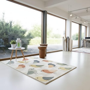 May include: A rectangular area rug with a checkered pattern and colorful bird illustrations. The birds are in shades of blue, yellow, orange, and gray. The rug is on a white floor in a bright room with large windows.