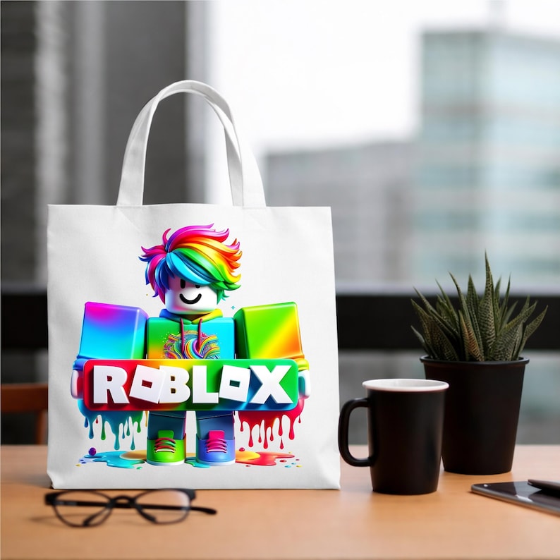 May include: White tote bag with a colourful Roblox character design. The character has rainbow hair and the word "ROBLOX" in a vibrant, dripping paint style. The bag has white handles. The bag is on a wooden table.