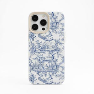 Puede incluir: Funda de teléfono blanca con un patrón azul toile de Jouy que representa escenas de árboles, personas y edificios. El área de la cámara tiene un borde beige. La funda está diseñada para un smartphone.