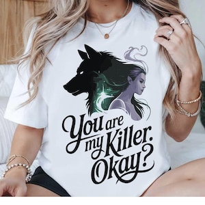 May include: White t-shirt with a graphic of a black wolf head, a woman's profile, and the text "You are my Killer. Okay?" in a decorative font. The design includes green and purple details.