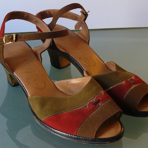 May include: A pair of vintage open-toe sandals with ankle straps. The shoes feature a color block design with olive green, red, and brown suede panels. The heels are a medium height, and the straps have gold-colored buckles. The soles are black.