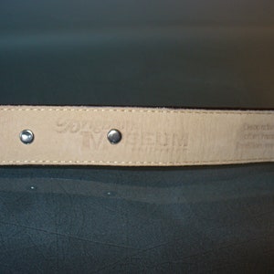 Pu&ograve; includere: Primo piano di una cintura in pelle marrone con rivetti color argento. L'interno della cintura &egrave; di colore beige chiaro con testo in rilievo. La cintura fa parte della "Museum Collection".