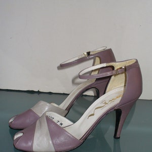 May include: A pair of lavender and cream-colored open-toe high heels with ankle straps. The heels have a pointed toe and a stiletto heel. The shoes are size 7 M. The brand name "Nina" is visible on the insole.