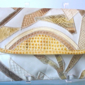 May include: A rectangular clutch bag featuring a patchwork design of cream-coloured smooth panels and textured, scale-patterned leather pieces in shades of tan, yellow, and brown, all joined together with visible zigzag stitching along the edges.