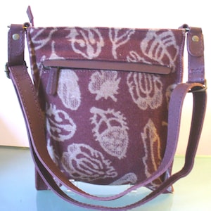 May include: A burgundy crossbody bag with a floral pattern in off-white. The bag features a zippered pocket, a matching adjustable strap, and leather accents. The bag is designed for everyday use.