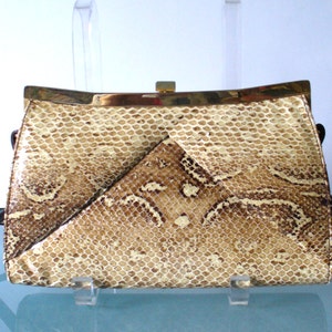 May include: A rectangular clutch bag featuring a tan and brown snakeskin pattern with a textured scale finish. The bag has a gold-toned metal frame along the top edge and a central rectangular clasp closure, presenting a structured and sleek appearance.