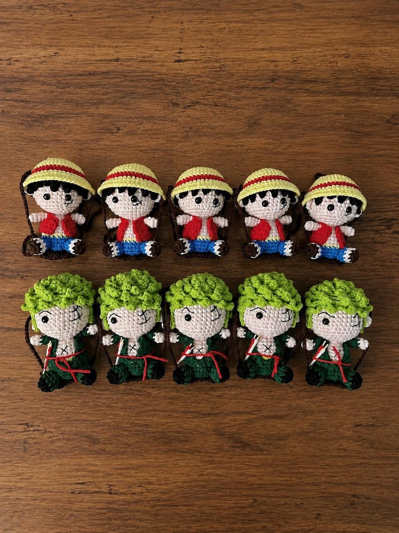 May include: Ten handmade crochet dolls. Five dolls are dressed in red vests, blue shorts, and yellow straw hats. The other five dolls have green hair and are dressed in green outfits. All dolls have black eyes and are on a brown background.