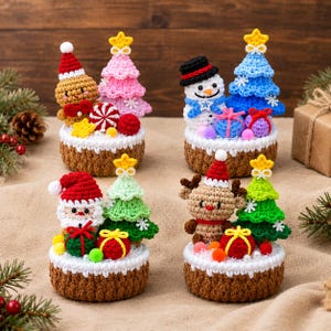 May include: Four crochet Christmas-themed displays on brown bases. Each features a character like a gingerbread person, snowman, Santa, or reindeer, paired with a colorful crocheted tree, small wrapped gifts, and decorative pom-poms.