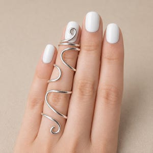 Könnte beinhalten: Ein silberner Fingerring mit einem durchgehenden, geschwungenen Drahtdesign, das sich in mehreren Schleifen um den Finger wickelt. Das Metall hat eine glatte, polierte Oberfläche und die Struktur besteht aus einem einzigen, gebogenen Silberdraht.